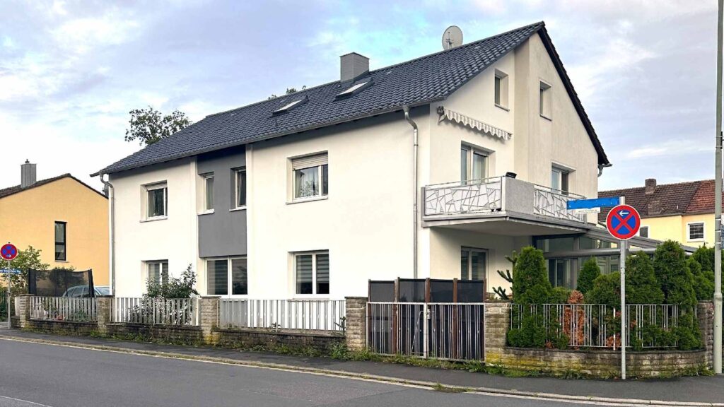 Modernes Einfamilienhaus mit heller Putzfassade, dunklem Ziegeldach und Balkon in Wohnstraße