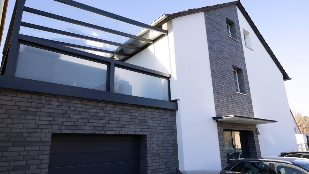 Modernes Einfamilienhaus mit grauer Klinkerriemchenfassade und weißer WDVS-Fassade, Glasüberdachung über Terrasse