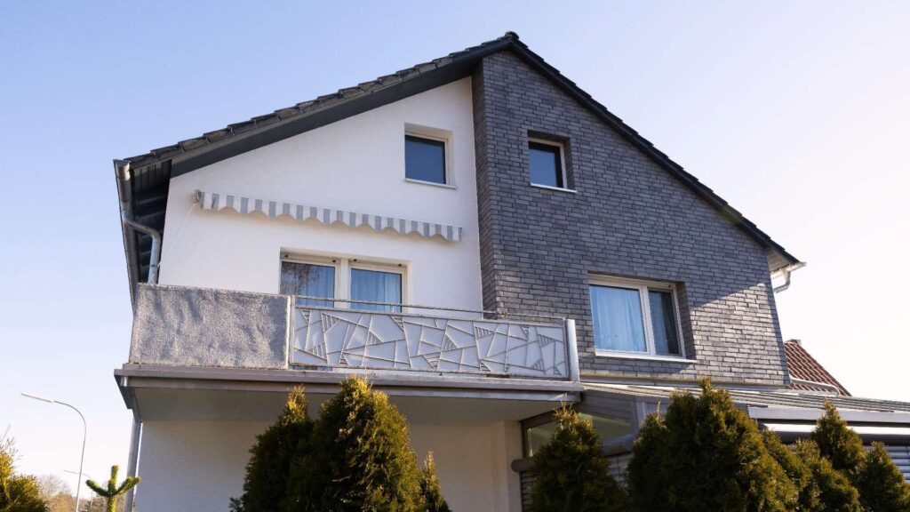 Modernes Einfamilienhaus mit zweifarbiger Hausfassade aus weißem WDVS und grauer Klinkerriemchenfassade mit Balkon