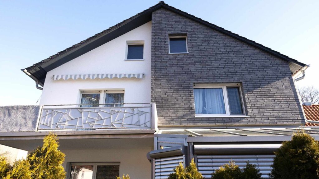 Modernes Einfamilienhaus mit zweifarbiger Hausfassade aus weißem WDVS und grauer Klinkerriemchenfassade, Balkon und Terrasse.