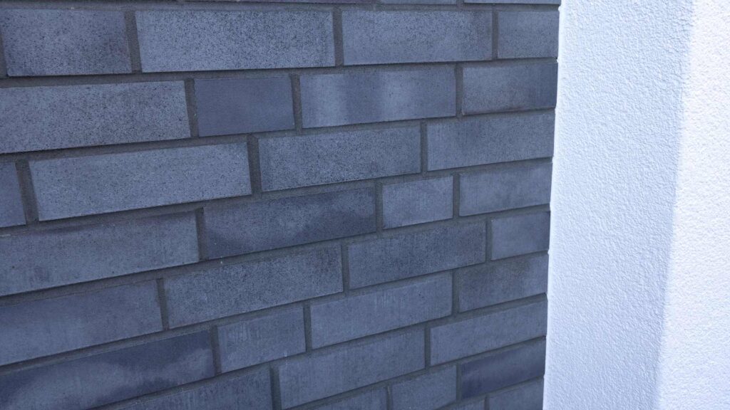 Moderne Hausfassade mit blauer Klinkerriemchenfassade und weißer Putzecke im Detail