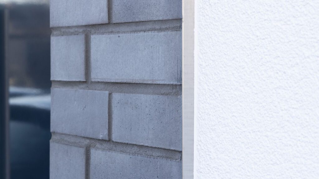 Detailansicht einer modernen Hausfassade mit grauen Klinkerriemchen und weißer Wandecke im Hintergrund.