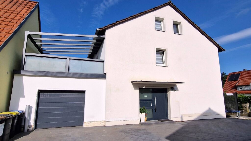 Moderne weiße Hausfassade mit WDVS, Garage und Balkon unter blauem Himmel in Wohngebiet