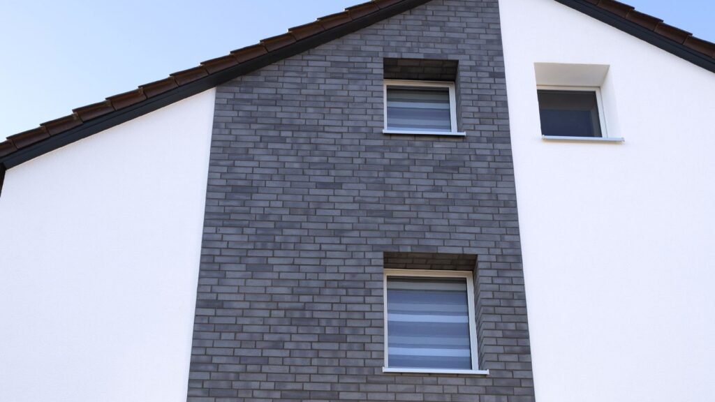 Moderne Hausfassade mit grauer Klinkerriemchenfassade und weißem WDVS, zwei Fenster übereinander angeordnet.