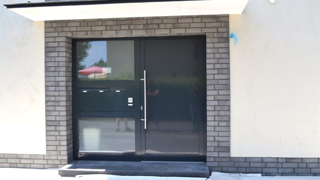 Moderne Hausfassade mit Klinkerriemchen und großer Glas-Eingangstür mit schwarzem Rahmen und Edelstahlgriff.