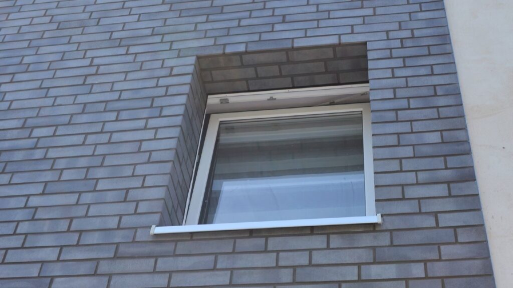 Ein geöffnetes weißes Fenster in einer modernen Klinkerriemchenfassade mit hellgrauen Steinen im Läuferverband.