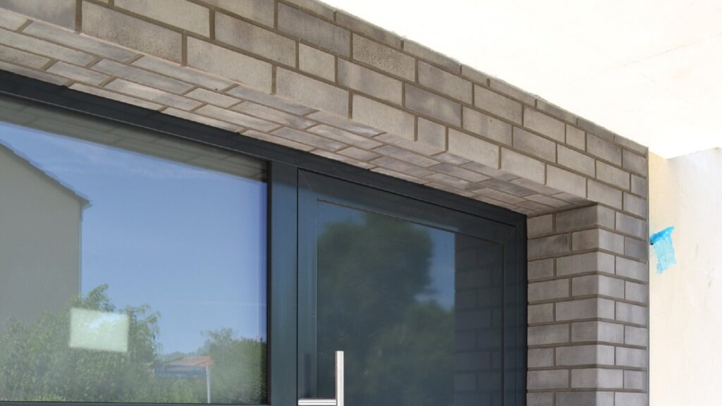 Moderne Hausfassade mit Klinkerriemchen und großen Fenstern mit dunklen Rahmen an einem Neubau.