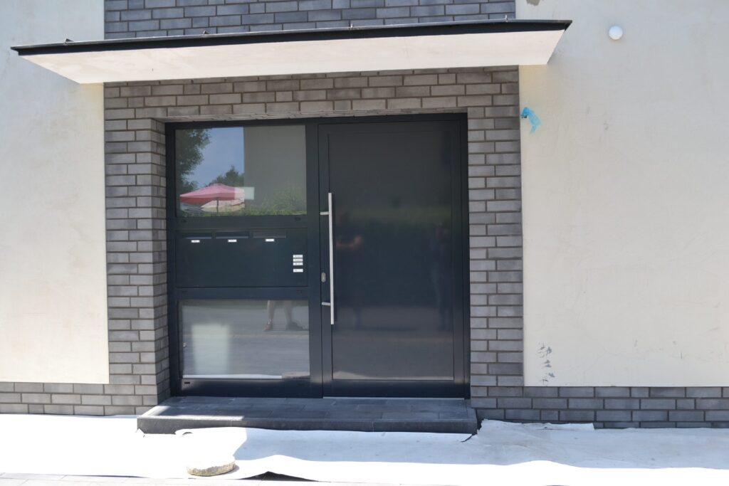 Moderne Hausfassade mit Klinkerriemchen und großer Glastür, überdacht von schmalem Vordach