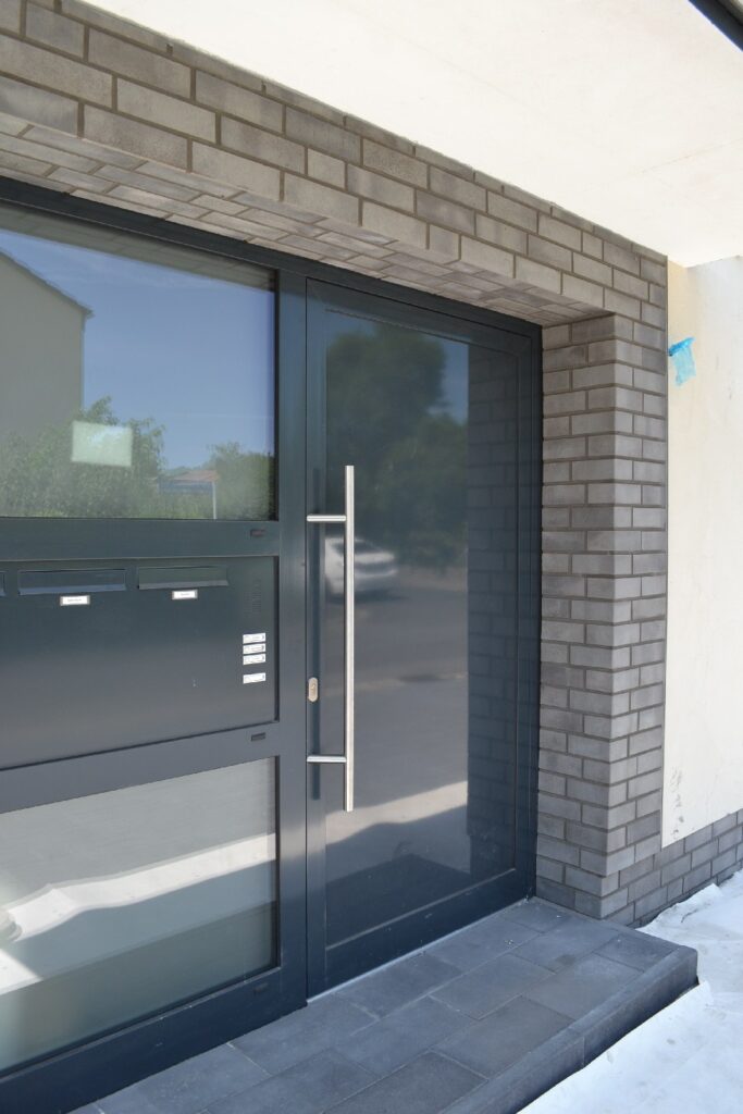 Moderne Hausfassade mit Klinkerriemchen und anthrazitfarbener Eingangstür mit großer Glasfront und Briefkästen