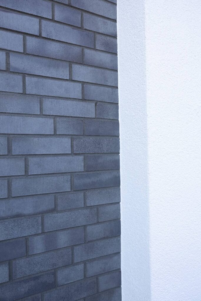 Moderne Hausfassade mit grauer Klinkerriemchenfassade neben weißer WDVS-Dämmung an Gebäudeecke