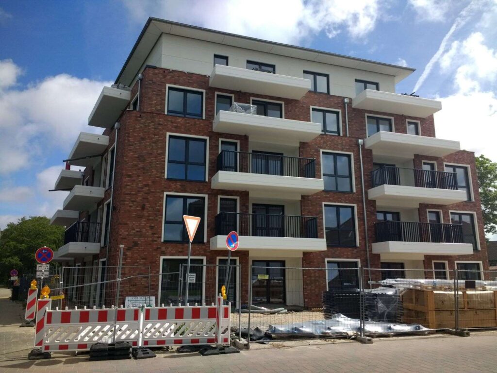 Moderner Neubau mit Klinkerriemchenfassade und weißen Balkonen, Baustelle mit Absperrungen davor