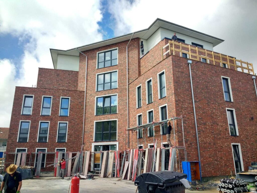 Neubau mit Klinkerriemchenfassade im Rohbau, Baugerüst und Baumaterialien vor modernem Mehrfamilienhaus