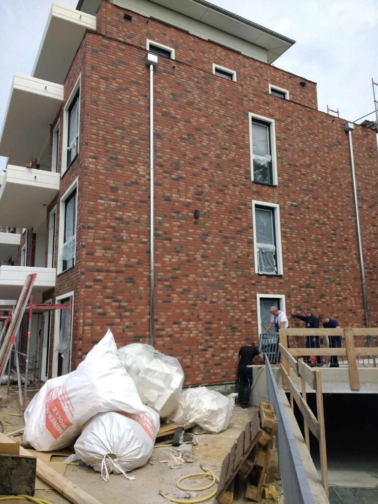 Baustelle mit Klinkerriemchenfassade und WDVS-Dämmung, Arbeiter installieren Fassadenelemente an modernem Wohngebäude