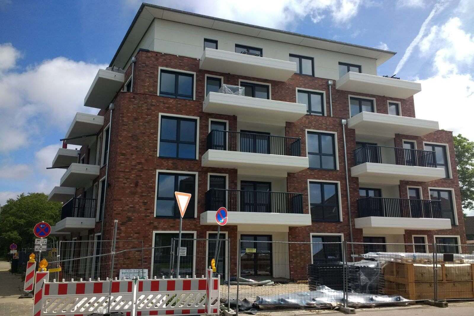 Neubau-Mehrfamilienhaus mit moderner Klinkerriemchenfassade und weißen Balkonen in Baustellenbereich