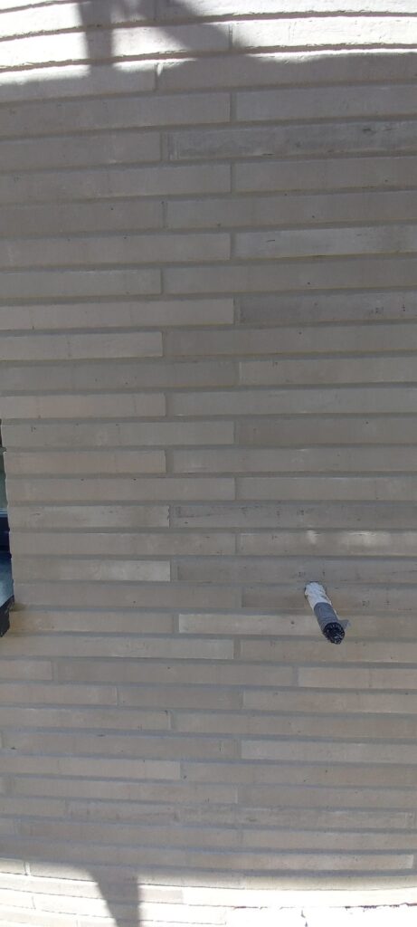 Klinkerriemchenfassade in hellen Grautönen mit versetztem Fugenbild und Schatten von Balkonelementen
