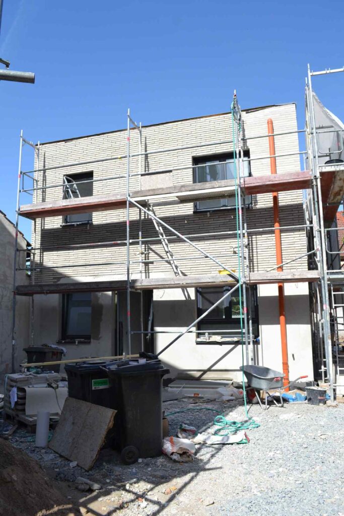 Hausfassade im Bau mit Klinkerriemchenfassade, umgeben von Baugerüst und Baumaterialien auf der Baustelle