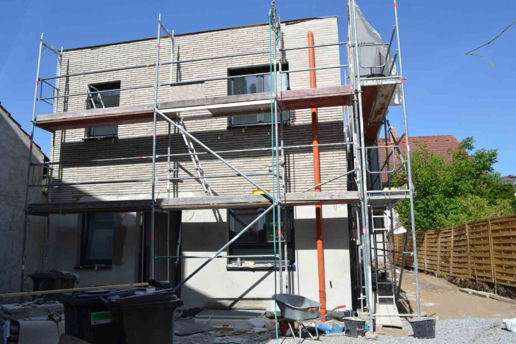 Neubau mit Klinkerriemchenfassade im Rohbau, umgeben von Baugerüst während der Fassadendämmung