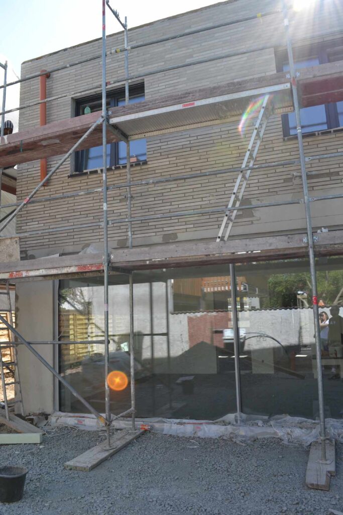 Baustelle mit Gerüst vor zweistöckigem Haus während Fassadendämmung, Klinkerriemchenfassade im oberen Bereich sichtbar