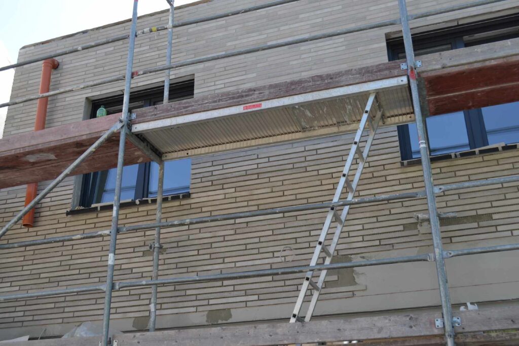 Bauarbeiten an einer Klinkerriemchenfassade mit Gerüst und Leiter vor einem mehrstöckigen Wohngebäude