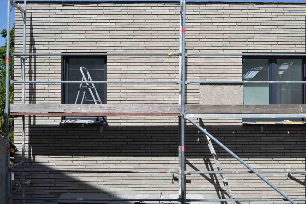 Baugerüst vor moderner Klinkerriemchenfassade mit Fenstern, Leiter auf Gerüstebene während Fassadenarbeiten