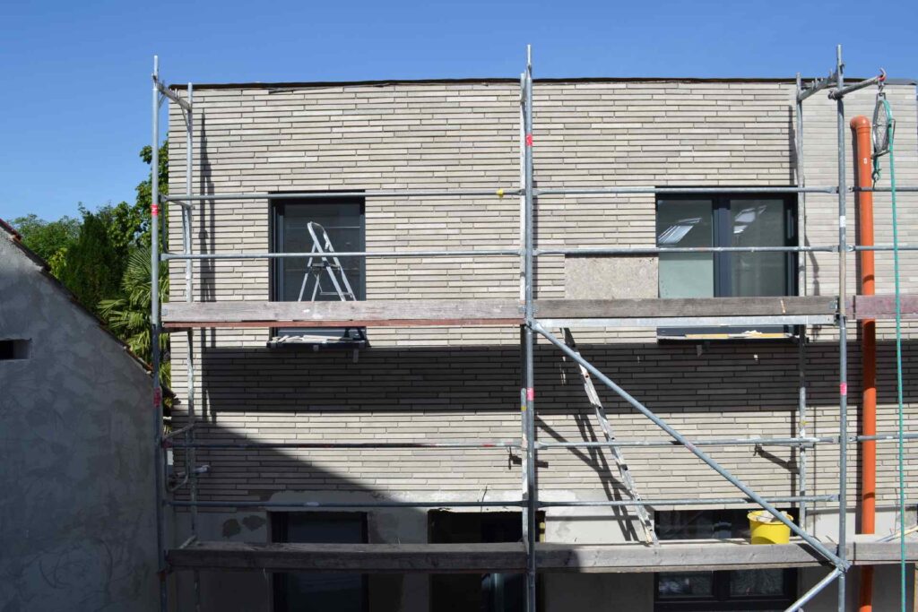 Hausfassade mit Klinkerriemchen im Bau, Gerüst und Fassadendämmung sichtbar, modernes Einfamilienhaus