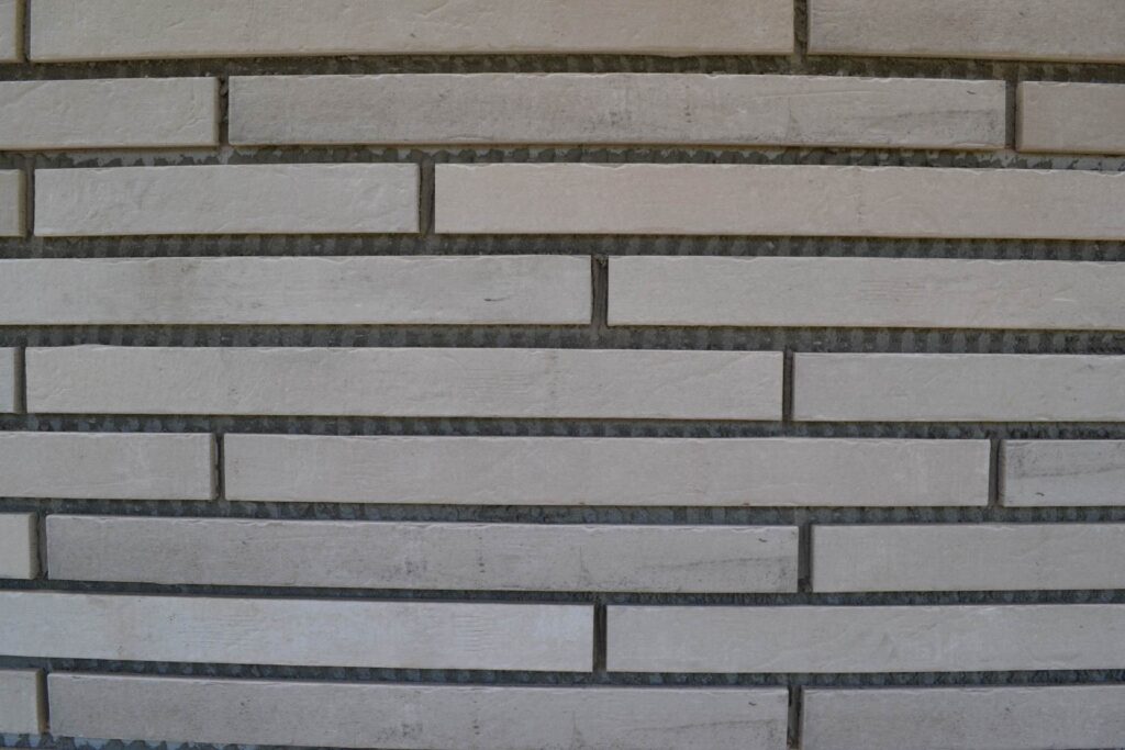 Moderne Klinkerriemchenfassade mit hellen, rechteckigen Steinen in versetztem Muster und dunklen Fugen.