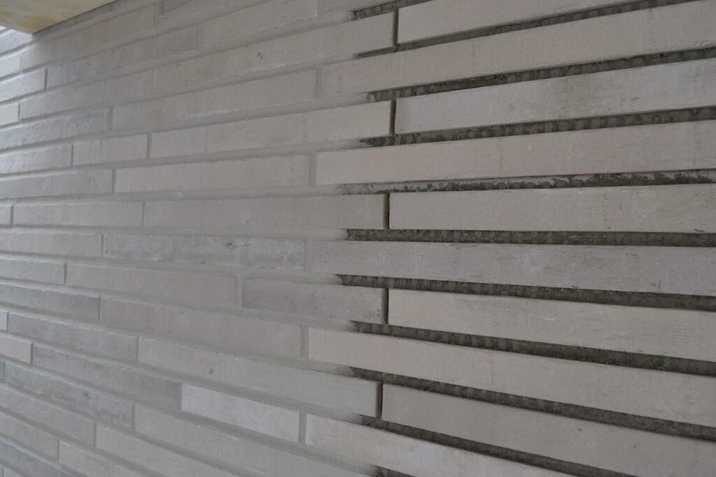 Hausfassade mit weißen Klinkerriemchen in unterschiedlichen Formaten und grauen Fugen während der Montage
