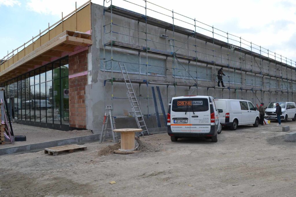 Baustelle mit Rohbau und Gerüst, Arbeiter verlegen Klinkerriemchen an der Hausfassade, Baufahrzeuge vor Ort