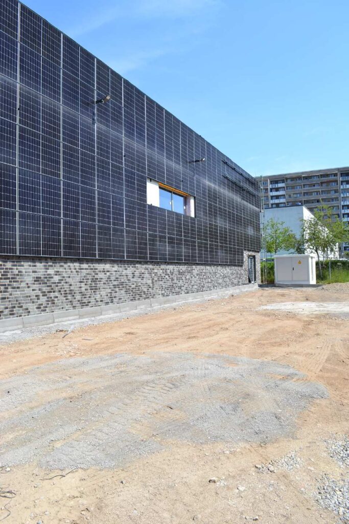 Modernes Gebäude mit Klinkerriemchenfassade im Sockelbereich und Solarmodulen, Baustelle im Vordergrund