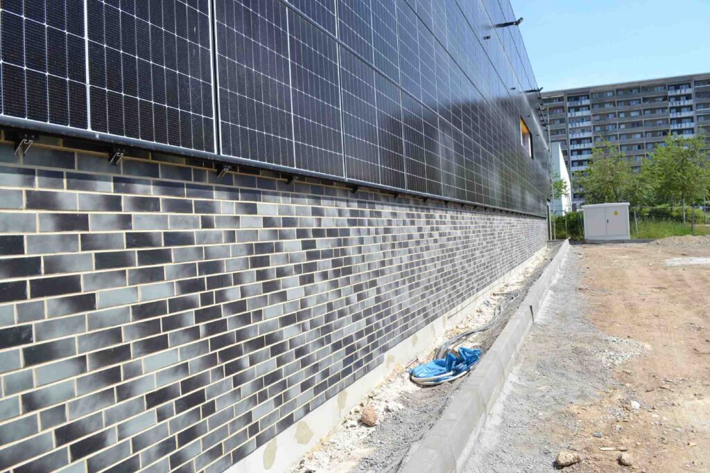 Klinkerriemchenfassade an Neubau mit Photovoltaikanlage, dahinter Wohnhochhaus und Baustelle