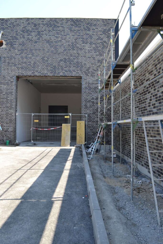 Baustelle mit Klinkerriemchenfassade und Gerüst, Eingangsbereich im Rohbau mit Absperrung
