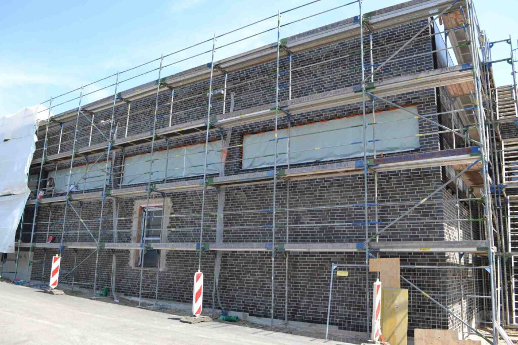 Baustelle mit Gerüst vor Klinkerriemchenfassade während Fassadendämmung und Renovierungsarbeiten am Wohnhaus
