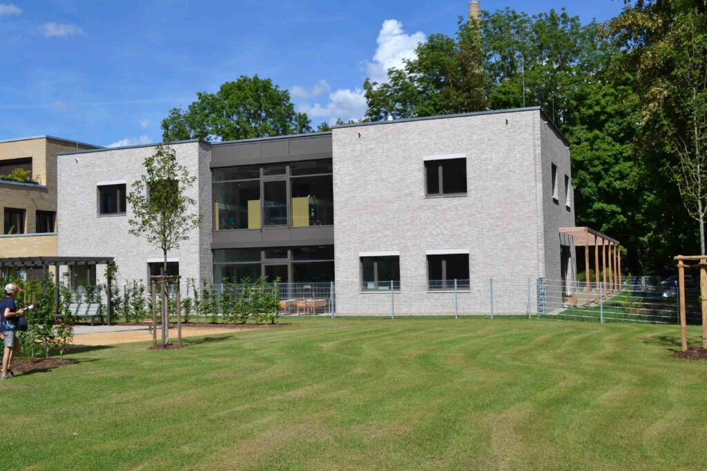 Moderne Hausfassade mit heller Klinkerriemchenfassade, großen Fenstern und gepflegtem Garten im Vordergrund