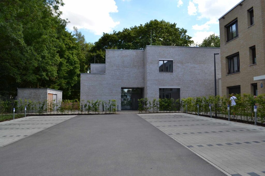 Moderne Wohnhäuser mit grauer Klinkerriemchenfassade und großen Fenstern, umgeben von Grünflächen und Bäumen.