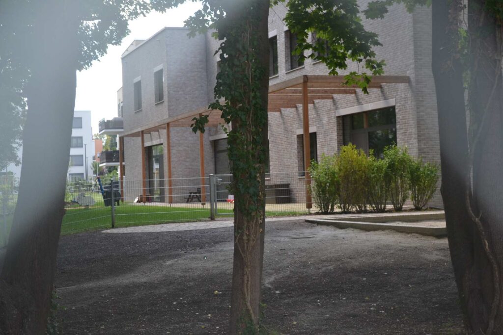 Moderne Wohnhäuser mit Klinkerriemchenfassade und Holzelementen, umgeben von Bäumen und gepflegter Gartenanlage.