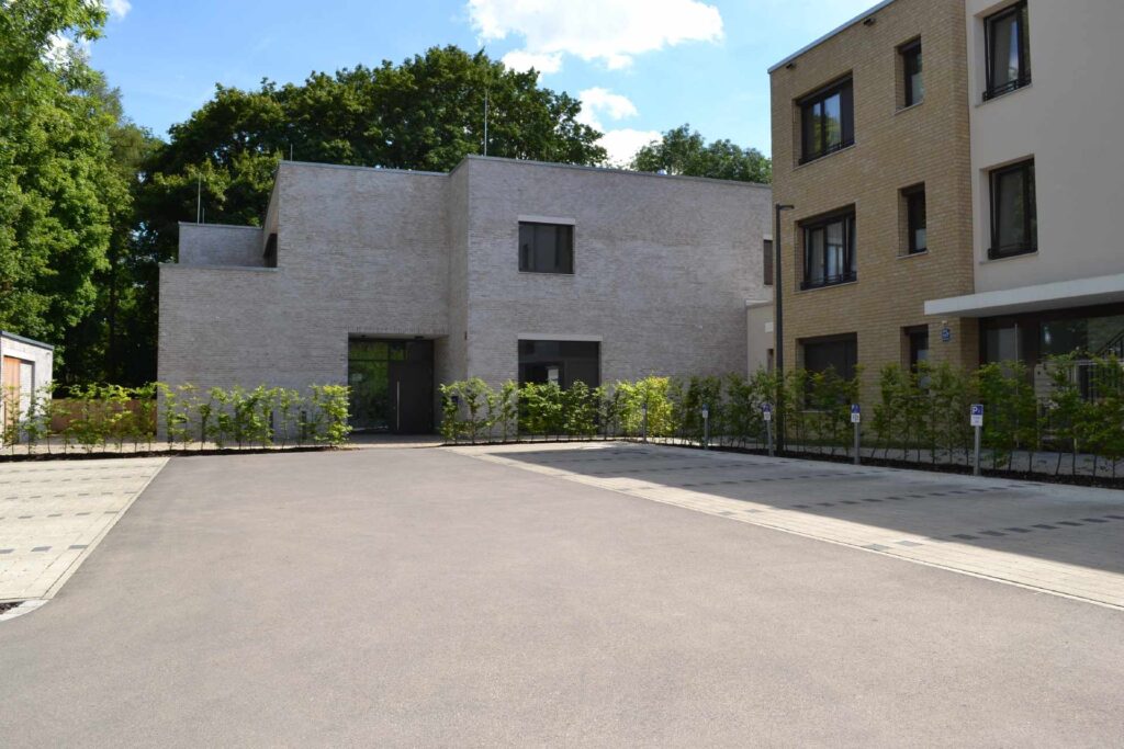 Moderne Wohnsiedlung mit grauer Klinkerriemchenfassade und gelbem Ziegelhaus, umgeben von Grünflächen