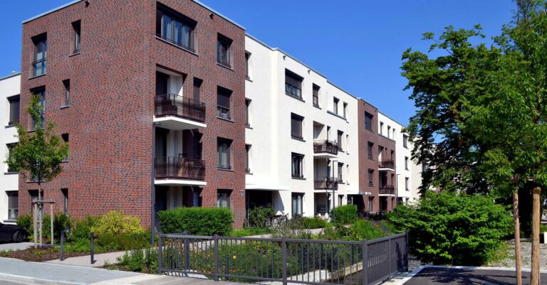 Moderne Wohnanlage mit Klinkerriemchenfassade und weißen WDVS-Elementen, umgeben von grüner Landschaftsgestaltung