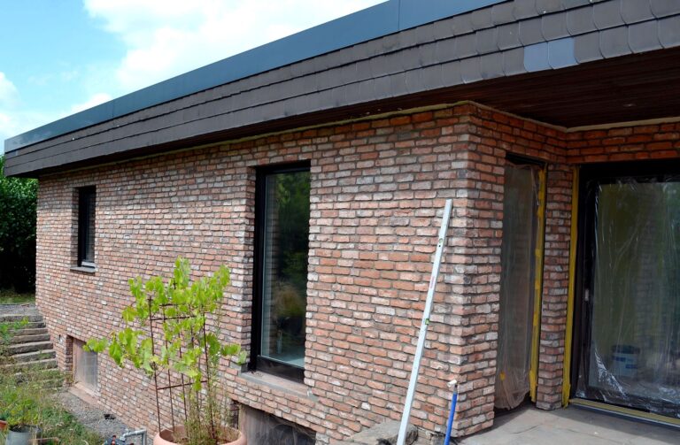 Modernes Einfamilienhaus mit Klinkerriemchenfassade und großen Fenstern, Baustelle mit Leiter und jungem Baum
