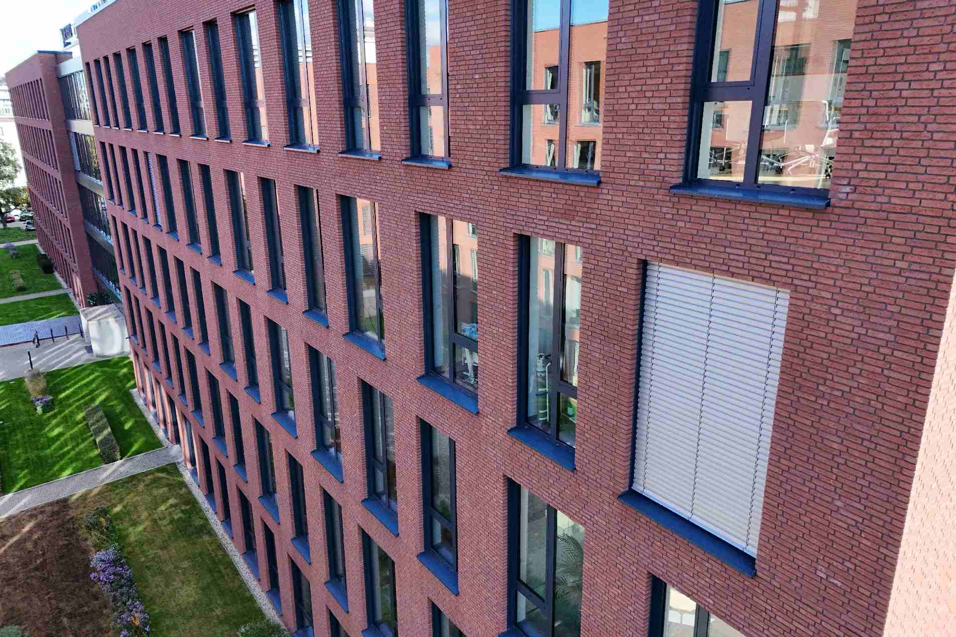 Moderne Hausfassade mit Klinkerriemchen und großen Fenstern, Blick auf mehrstöckiges Wohngebäude mit Grünfläche