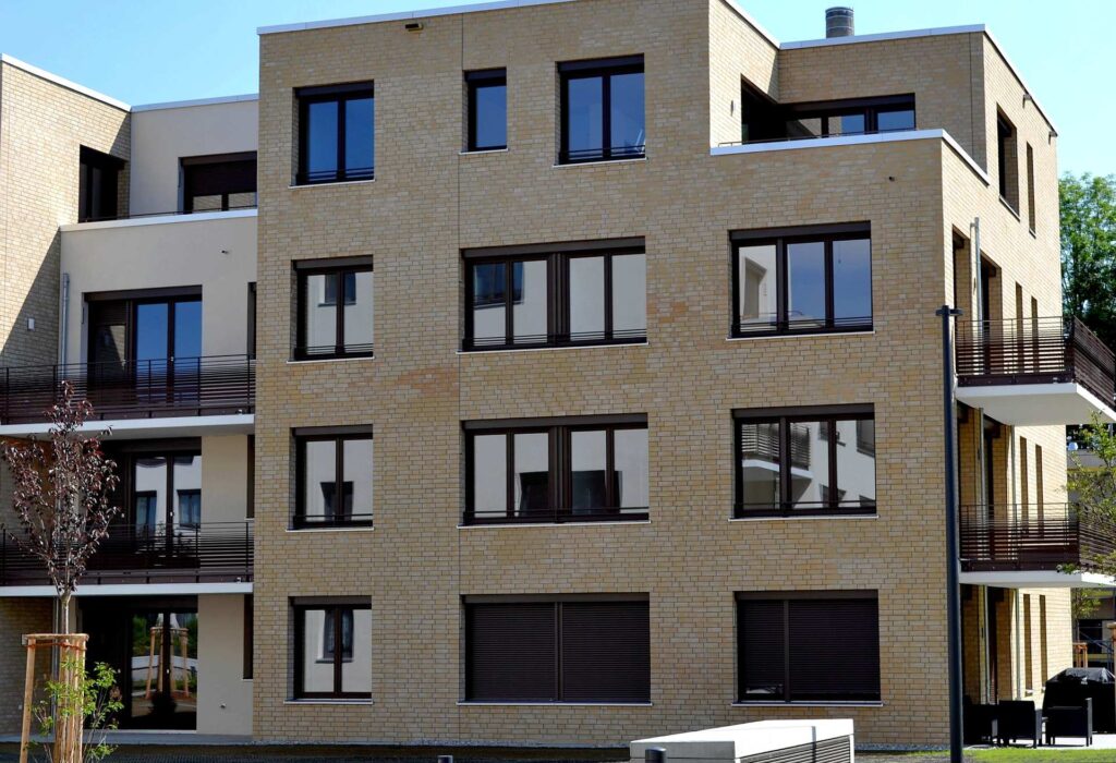 Moderní bytový dům s klinkerovou páskovou fasádou a tmavými okny s balkonem v přízemí