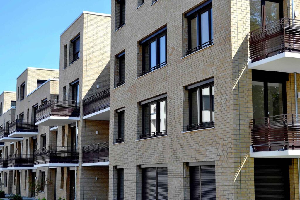 Moderní bytový dům s klinkerovou páskovou fasádou a balkony s dřevěným zábradlím pod modrou oblohou
