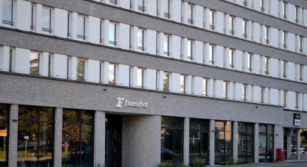 Moderní bytový dům s klinkerovou páskovou fasádou a velkými okny, přízemí s obchody Fitness First