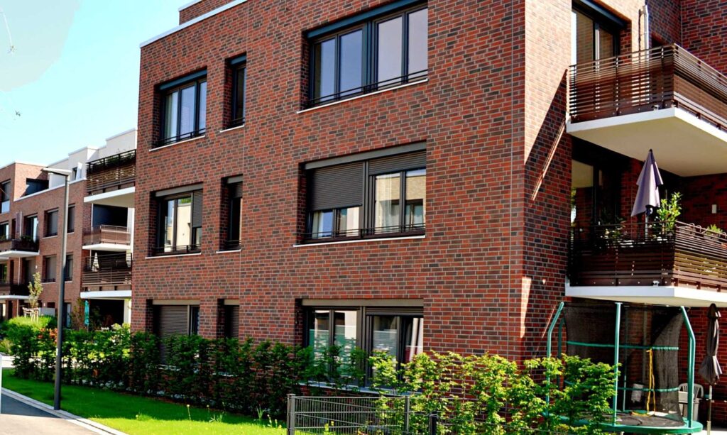 Moderní bytový dům s klinkerovou páskovou fasádou a balkony s dřevěným obložením v rezidenční čtvrti