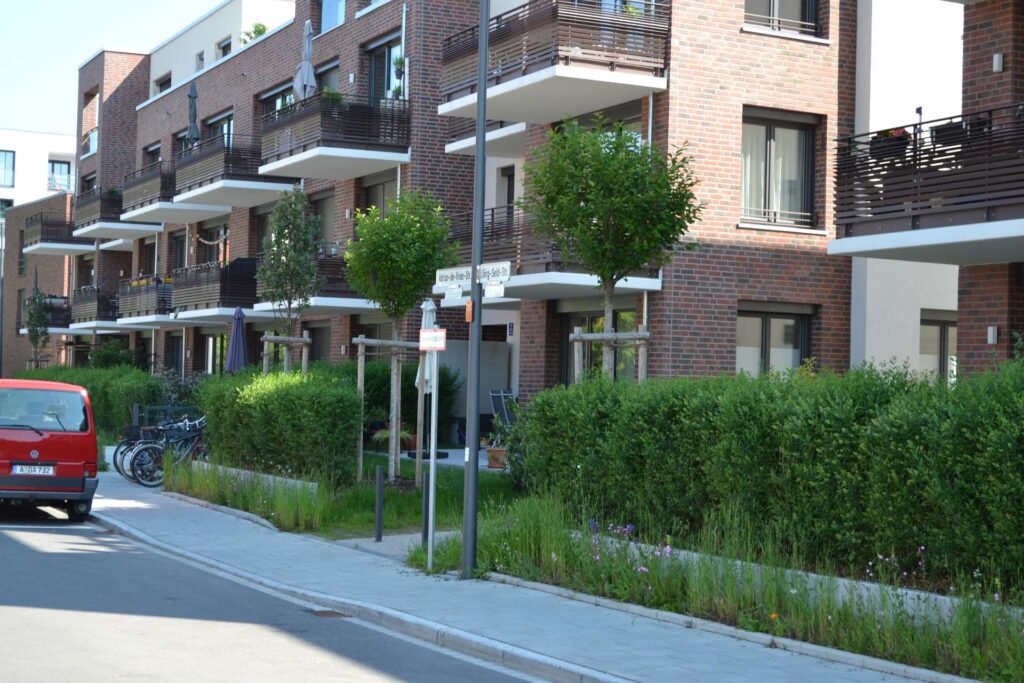 Moderní bytový dům s klinkerovou páskovou fasádou, balkony s dřevěným obložením a zelení před budovou