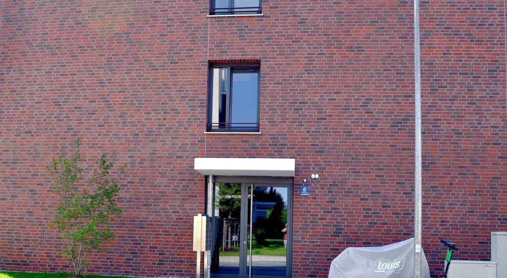 Moderní fasáda z klinkerových pásků s kontrastními okny a skleněnými dveřmi pod bílým přístřeškem.