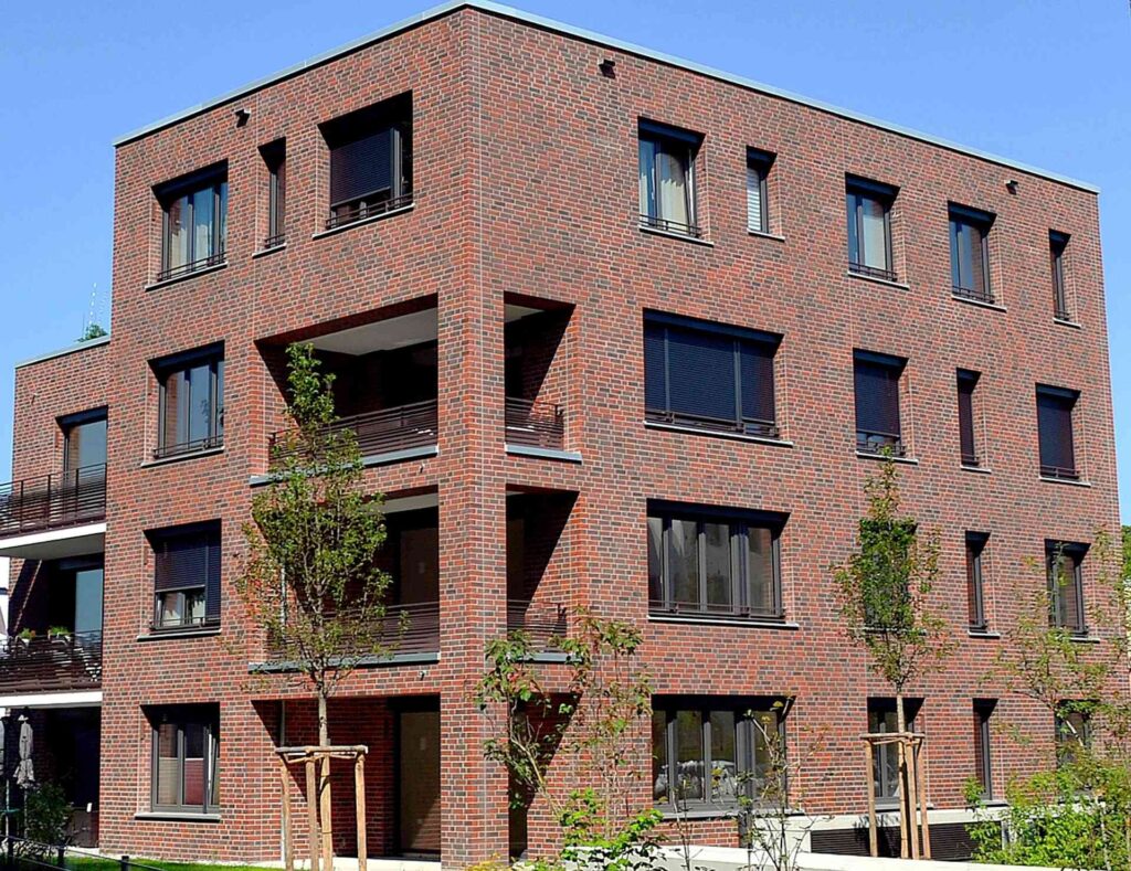 Moderní bytový dům s klinkerovou páskovou fasádou, balkony s kovovým zábradlím a velkými okny