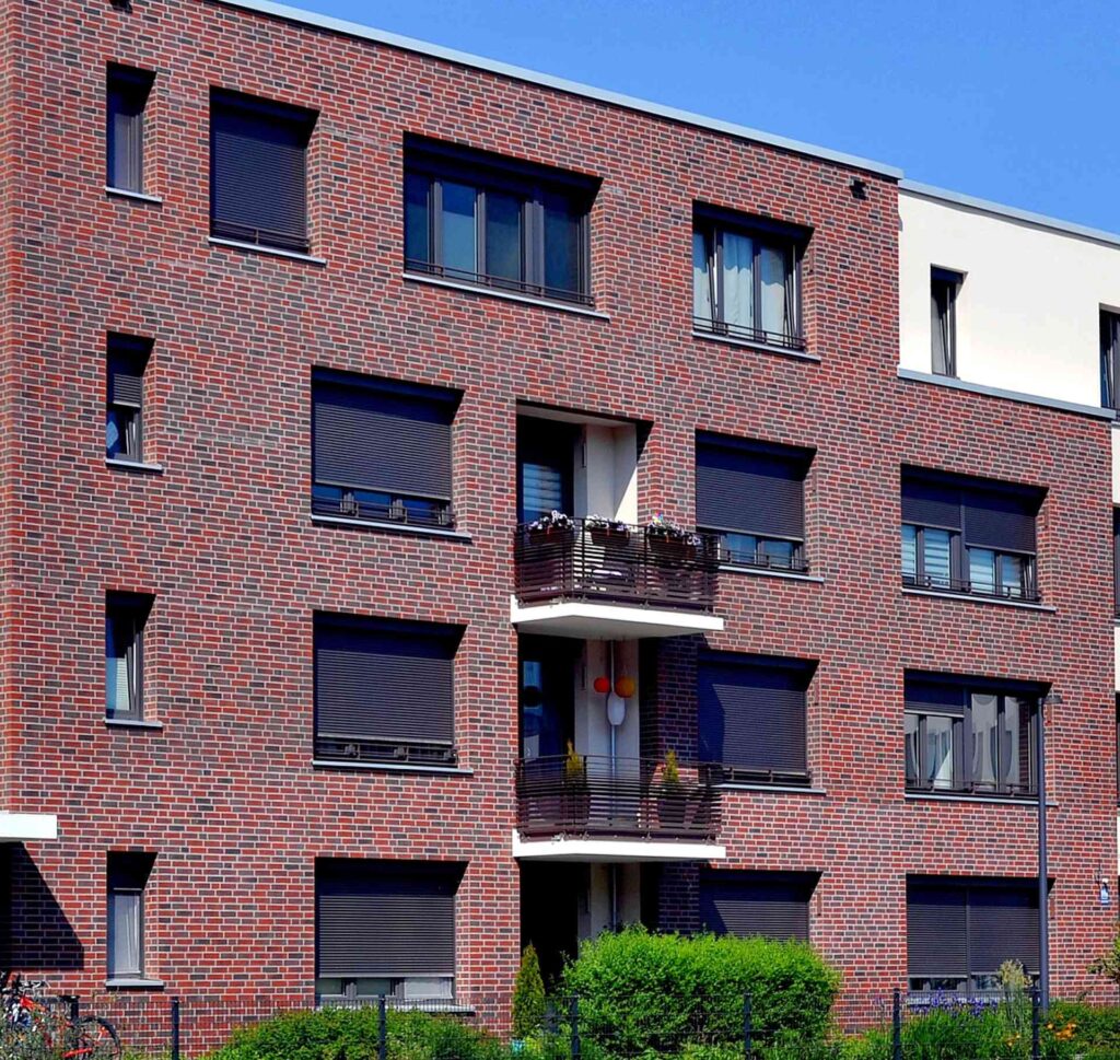 Moderní bytový dům s klinkerovou páskovou fasádou, balkony s roletami a zateplením