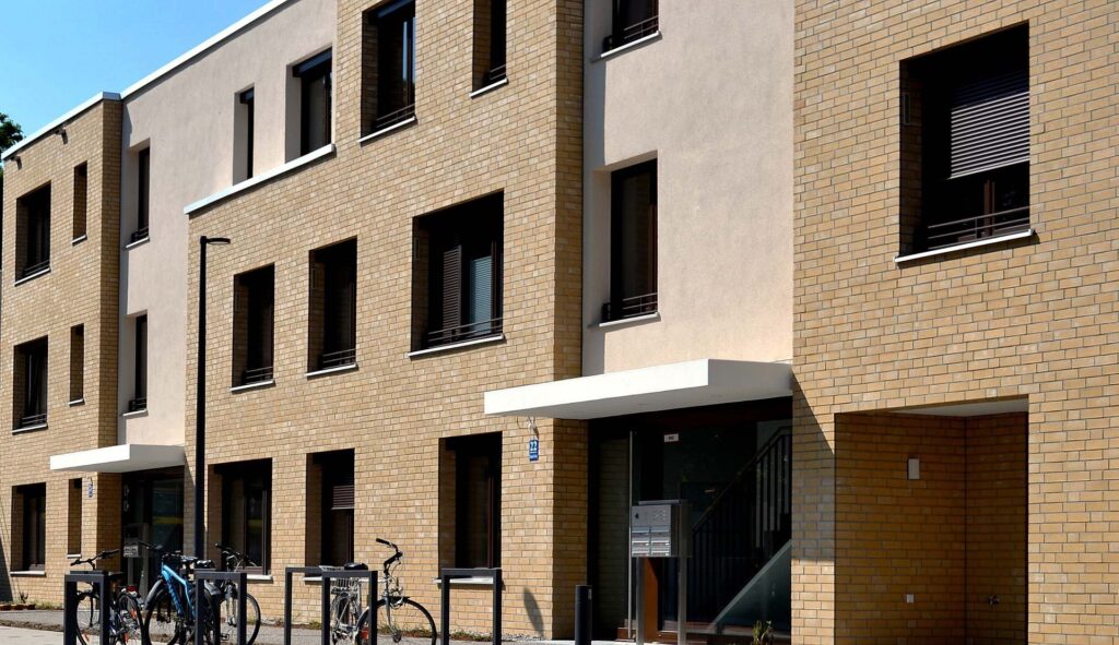 Moderní bytový dům s fasádou z klinkerových pásků a betonových prvků, před budovou stojan na kola