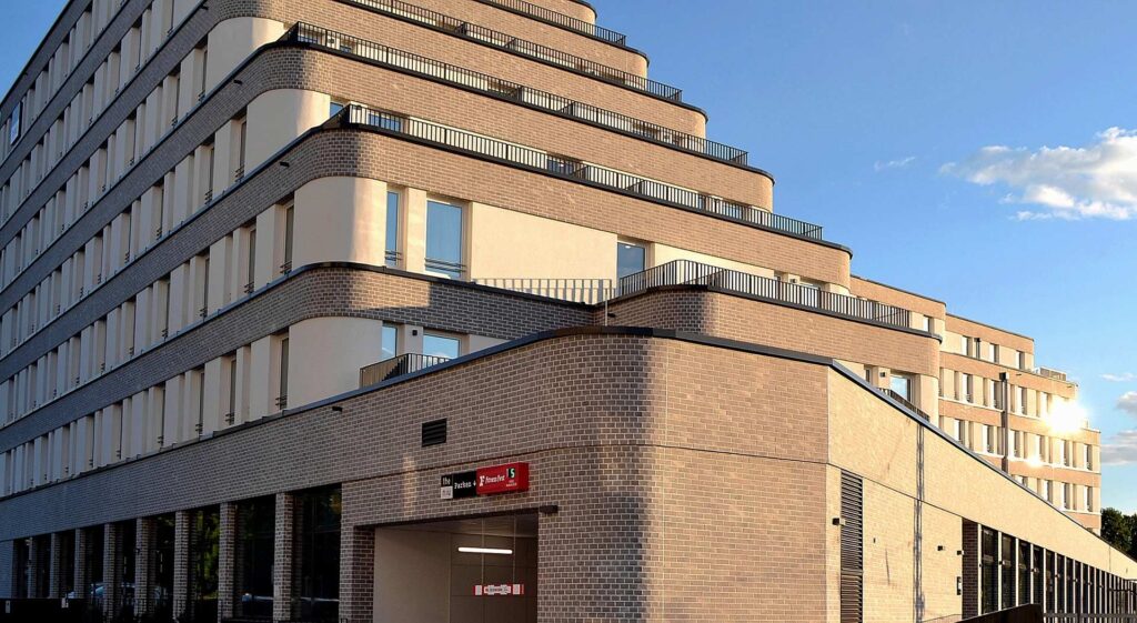 Moderní bytový dům s klinkerovou páskovou fasádou a zakřivenými balkony proti modrému nebi