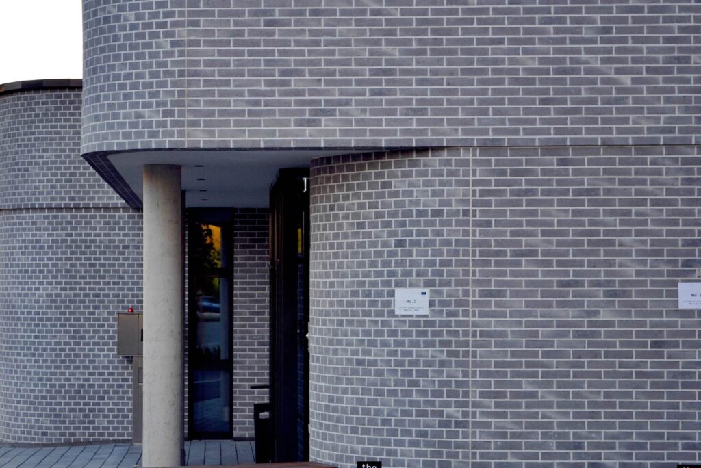 Moderní budova s fasádou z šedých klinkerových pásků a vstupním portálem s tmavým přístřeškem